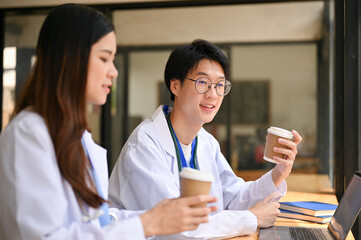 Two Asian doctors are having a quick lunch break at a cafe, talking and having coffee together.
