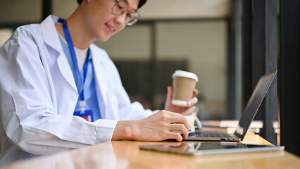 Cropped image of a smart young Asian male doctor reading a book at a cafe.