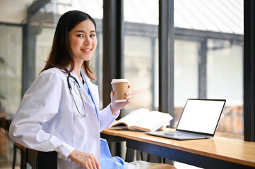 Beautiful Asian female doctor in a uniform has a coffee at a cafe for her lunch.