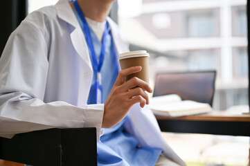 Cropped image of a male doctor sits in a cafe holding a takeaway coffee cup