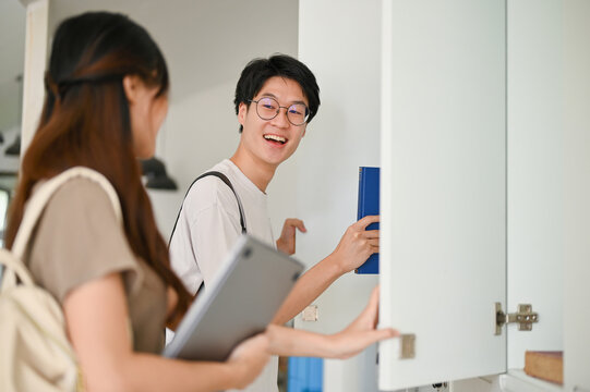 Cheerful Asian male college student talking with his friend at a school corridor.