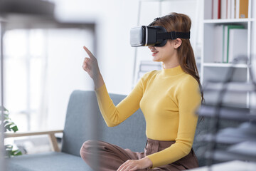 Surprised Young latin or asian woman in VR headset touching air, Smiling white woman wearing vr glasses while sitting on sofa at home.