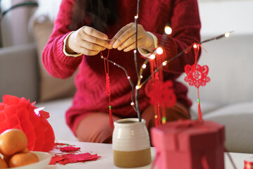 Asian Woman decorated house for Chinese New Year Celebrations. putting traditional pendant to the...