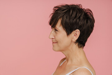 Fototapeta na wymiar Profile of senior woman smiling while standing isolated over pink background
