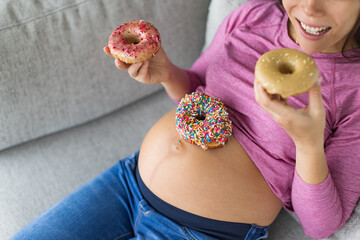 Pregnant woman eating sweet donuts on belly. Cravings of desserts and unhealthy food during pregnancy, Funny top view of cakes on baby bump for gestational diabetes or food cravings during pregnancy