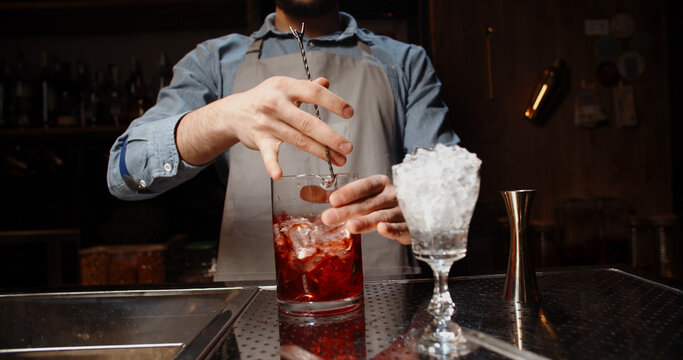 Professional bartender masterly creating a cocktail in modern bar. Experienced barman mixing red alcoholic beverage before serving - food and drink, nightlife close up 
