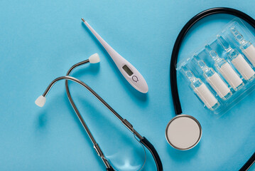 Collection of stethoscope, thermometer and ampoules with vaccine on blue background