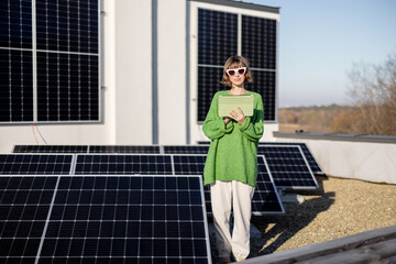 Young woman with a digital tablet monitors energy production from the solar power plant on rooftop...