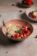 Oatmeal porridge with a spoon, berries and mint in a bowl on the table for a breakfast close-up.
