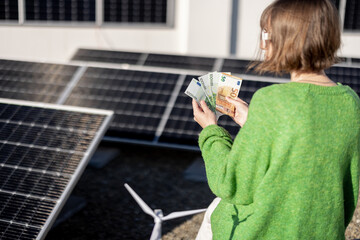 Woman counts euro banknotes saved due to the generation of energy from a solar power plant...