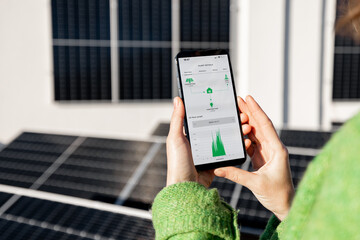 Woman monitors energy production from the solar power plant with mobile phone. Close-up view on phone screen with running program. Concept of remote control of solar energy production - 593463597
