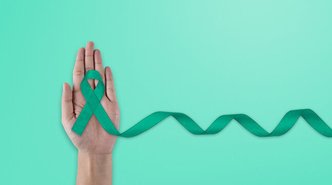 Hands holding emerald green or jade green ribbon on white fabric background with copy space, symbol for Liver Cancer awareness, World Cancer Day. Healthcare