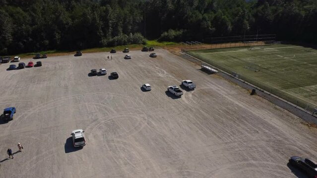A white pick up truck driving in circles, kicking up dust and making donuts at a fair or festival event in Squamish BC from an aerial view of the parking lot with a 4K drone.