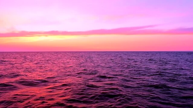 Beautiful sea waves with reflection of purple and pink sunset light glowing, by the beach with colorful sky clouds on the background, calm horizon scene, wide shot, slow motion, hd. ProRes 422 HQ.