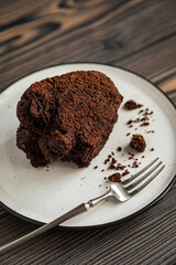 Close-up of piece of chocolate bundt cake, dessert fork on white plate on wooden table,