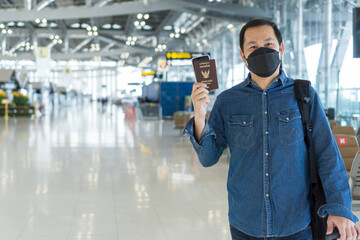 Asian male passenger wearing protective face mask showing passport book, text on that cover means "Thailand passport". Touris man showing boarding pass on mobile phone at airport. Travel concept.