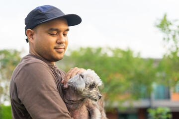 Yong asian man in casual outfit of cheerful with old dog at outdoors. Male playing with her little adopted dog pet and owner having good time together. Hugs and kisses, Love, Care, Friendship