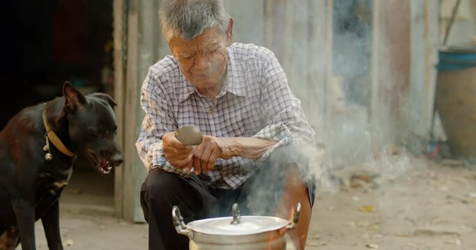 Slow motion Asian rural life in the evening sunset time which is a poor lonely elderly man, farmer and employee in the farm, cooking rice using a stove with firewood in front of his old house.
