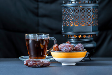 Dates, an oriental bowl with dates, a transparent cup with tea, a traditional lantern on a dark background
