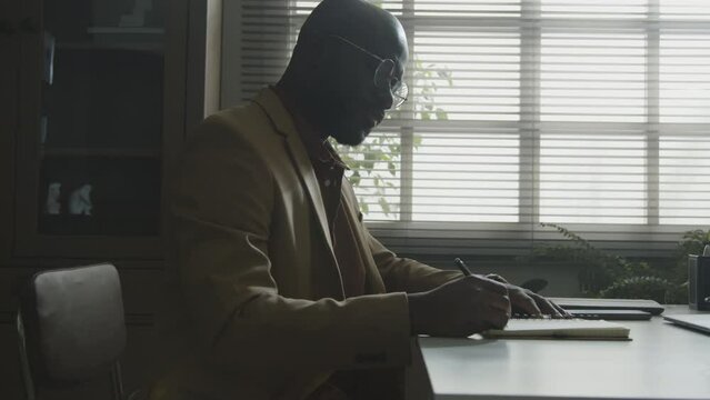 Psychologist sitting at desk writing in diary and checking the time