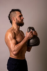 Young muscular man posing with a kettlebell on a light background.