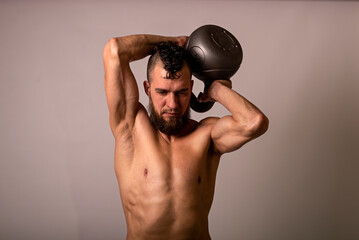 Young muscular man posing with a kettlebell on a light background.