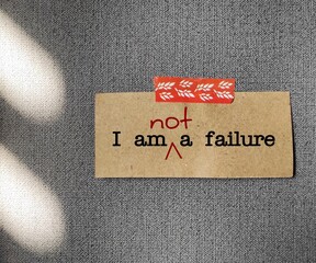 Red pencil correct message on note paper I AM A FAILURE changed to I AM NOT A FAILURE - affirmation self talk to challenge negative inner critic, replace with positive thought to raise self esteem