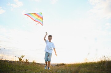 Boy is running with a kite during the day in the field