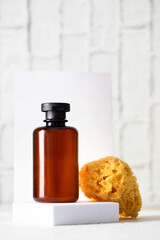 Abstract brown bottle on the podium and sea sponge at white tile bath background.
