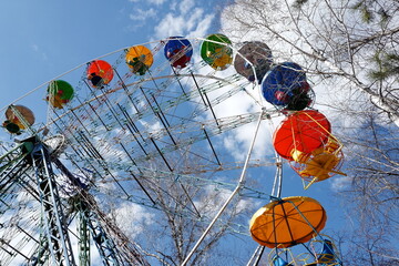 Ferris wheel in the cold season, trees without leaves, against the background of a sky with clouds