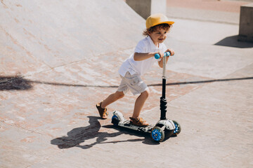 Cute little boy with curly hair riding scooter © Petro