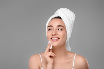Beautiful woman in terry towel removing makeup with cotton pad on gray background