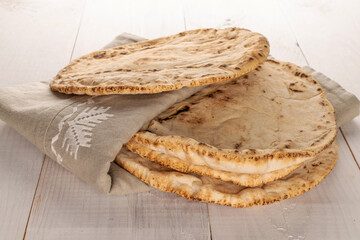 Four baked pita bread with linen napkin, close-up, on a wooden table.