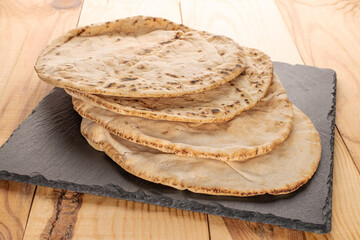 Four baked pita bread on a slate board, close-up, on a wooden table.