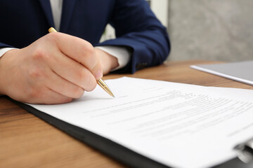 Man signing document at wooden table, closeup