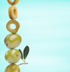 Cut and whole green olives with leaves on light blue gradient background, space for text