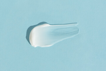 White cream texture on a blue background. A smear of a cosmetic skin care product. Wellness and beauty concept. Top view