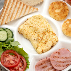 Breakfast plate. Omelet, cheesecakes, fried sausage, vegetables, herbs, toasted bread. Homemade breakfast. View from above. White background. Close-up.