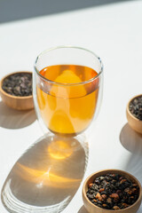 Different types of green, black and herbal tea in a wooden bowl and glass cup. Variety of dry leaves and flowers. Organic high-quality ingredients for a drink. Selective focus