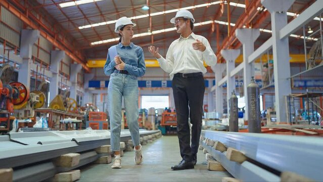 Two professional engineer man and woman manager leader wearing helmet walking in factory talking and discussing for work