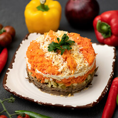 Layered salad with carrots, meat, vegetables, eggs on plate. Round salad bowl. Bright festive salad. Side view. Gray background. 