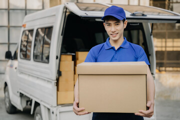 Asian delivery man portrait of young man holding cardboard box while unloading moving van outdoors.