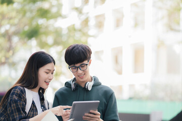 Obraz premium Asian college student reading a book study on laptop prepare for the exam Or work on a group project while sitting on the steps of the university.