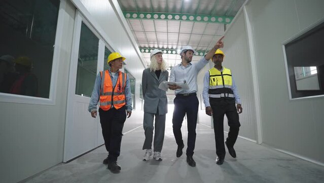 Group of factory warehouse workers walking and talking in warehouse for work wearing safety hardhats helmet inspection at warehouse