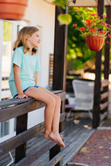 Cute sleepy girl sitting on the railing of the terrace of the house.