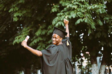 Portrait back view of happy black man graduate from university stand outdoors among trees and...