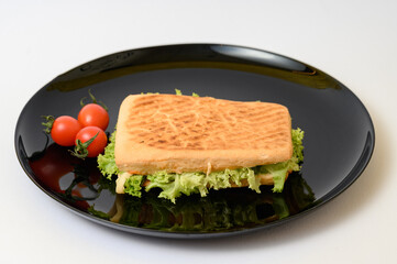 Cooked panini with green lettuce on a black plate with cherry tomatoes.