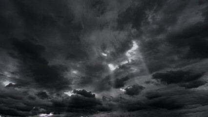 dark dramatic sky with black stormy clouds before rain or snow as abstract background, extreme weather, the sun shines through the clouds, high contrast photo