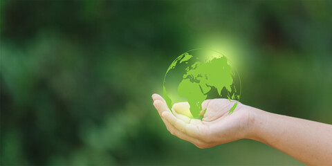 Human hand holding a green earth globe on blurred nature background, save the world concept