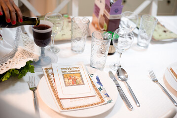 On white served traditional table with haggadah prepared for Passover with matza, egg,  wine, glasses and green salad. Spring Holiday of Jewish people. Fasting time